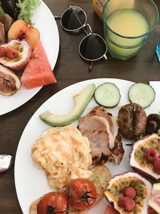 Breakfast of scrambled eggs, bacon, avocado, roast tomatoes on toast and passionfruit, with a fruit plate and juice